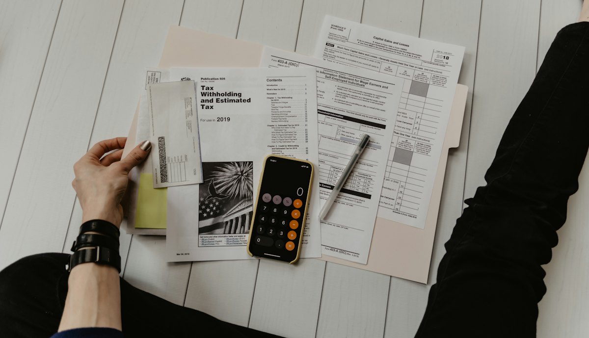 Tax forms, a calculator and a pen laid out on a desk